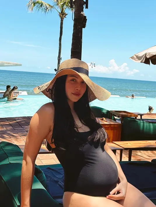 <p>Untuk look modis saat bersantai di beach club, Estelle Linden menambahkan straw hat dan swimsuit one piece warna hitam. [Foto: @estelleelinden]</p>