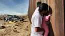 Seorang pria sambil menggendong bayi melepas rindu dengan kerabat dalam acara "Keep our dream alive" di dinding perbatasan antara Meksiko dan Amerika Serikat di Ciudad Juarez, negara bagian Chihuahua, 10 Desember 2017. (Herika MARTINEZ/AFP)