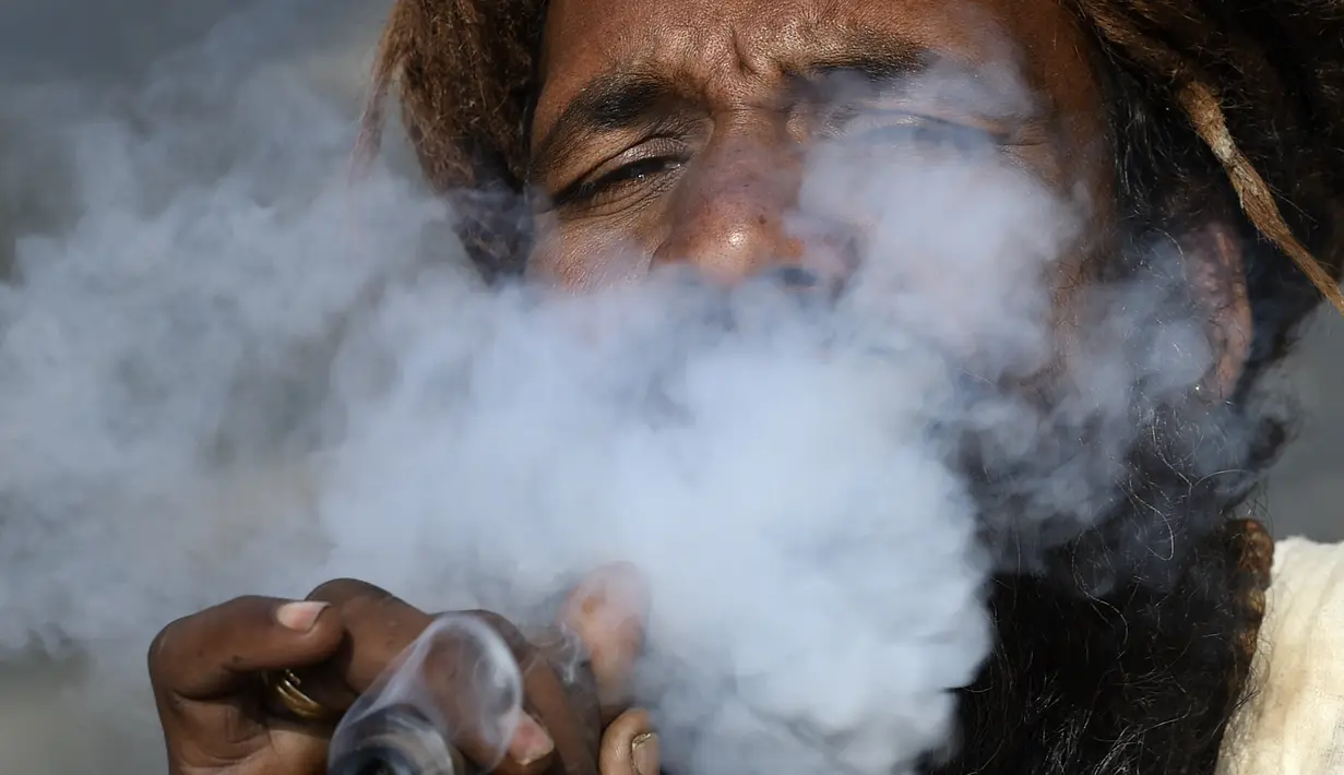 Seorang Sadhu atau orang suci Hindu menghisap ganja menggunakan 'chillum', pipa tanah liat tradisional, menjelang festival Hindu 'Maha Shivaratri', di Kathmandu (9/3/2021). Festival ini dirayakan sebagai bentuk persembahan kepada Dewa Siwa. (AFP/Prakash Mathema)