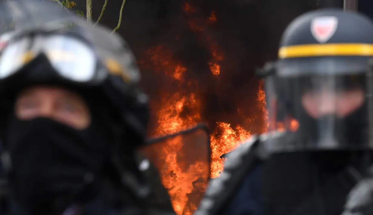 Polisi anti huru hara berjaga dengan latar belakang api yang menyala saat terjadi aksi demonstrasi pada peringatan Hari Buruh di Paris, Prancis (1/5). Hari Buruh yang jatuh pada tanggal 1 Mei ini diperingati di berbagai negara. (AFP/Alain Jocard)