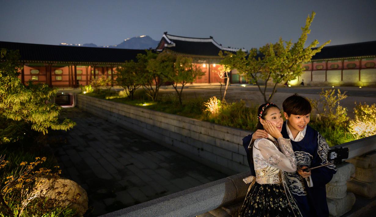 Pengunjung mengenakan gaun tradisional Korea, hanbok sambil berpose saat kunjungan malam ke Istana Gyeongbokgung di Seoul, 4 Oktober 2019. Kunjungan malam tersedia pada minggu ketiga dan keempat setiap bulan mulai dari 26 April sampai 31 Oktober, kecuali pada bulan Agustus. (Photo by Ed JONES / AFP)