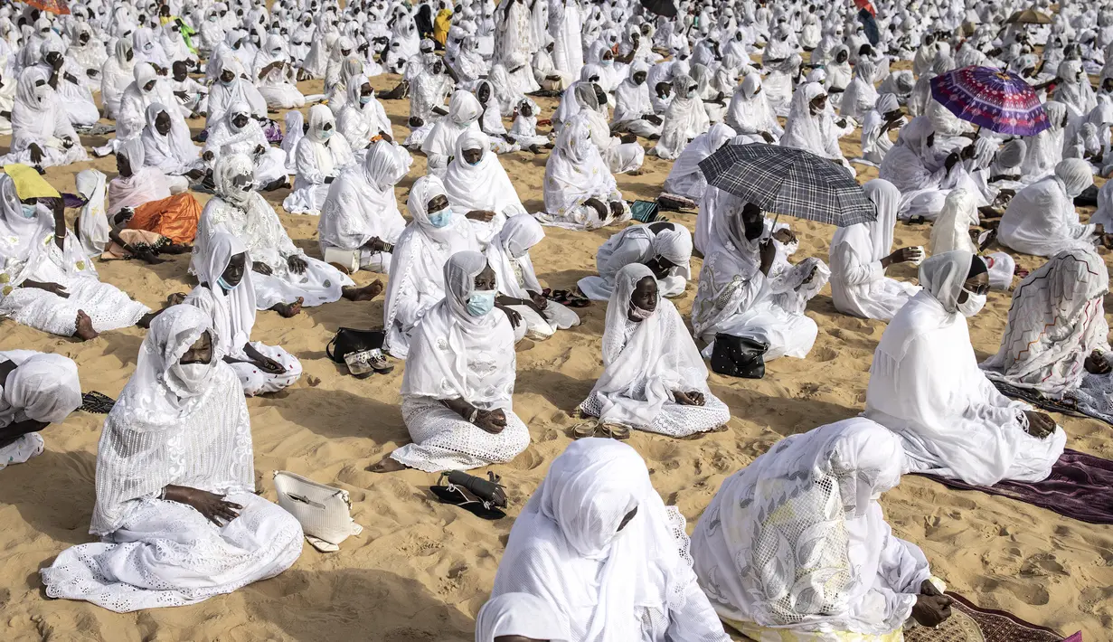 Pengikut komunitas Layene Senegal terlihat selama perayaan Tabaski (Idul Adha) di lingkungan populer Yoff di Dakar, Rabu (21/7/2021). Bendera putih kecil yang tertancap di atas pasir pantai Yoff terpasang sebagai penanda jaga jarak antar jemaah. (JOHN WESSELS / AFP)