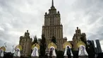 Orang-orang berjalan melewati "benda seni Matryoshki", tujuh boneka bersarang tradisional Rusia "matryoshka" dengan hiasan kepala "kokoshnik", di depan gedung pencakar langit era Soviet "Ukraina" hotel di pusat kota Moskow (9/9/2021).  (AFP/Kirill Kudryavtsev)