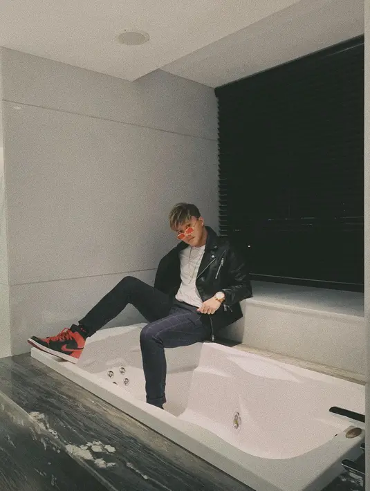 Penampilannya simple Rizky dengan mengenakan jaket kulit berwarna hitam dan kaus bewarna putih. Rizky berpose ala model dengan duduk di bathtup dengan mengenakan celana jeans berwarna hitam. Sepatu Jordan berwarna merah berpadu hitam dan putih tampak membalut kakinya.(Liputan6.com/IG/@rizkyfbian)
