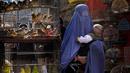 <p>Seorang perempuan mengenakan burqa berjalan melalui pasar burung saat dia menggendong anaknya, di pusat kota Kabul, Afghanistan, 8 Mei 2022. Taliban memerintahkan perempuan Afghanistan untuk mengenakan pakaian dari kepala hingga ujung kaki atau burqa tradisional di depan umum. (AP Photo/Ebrahim Noroozi)</p>