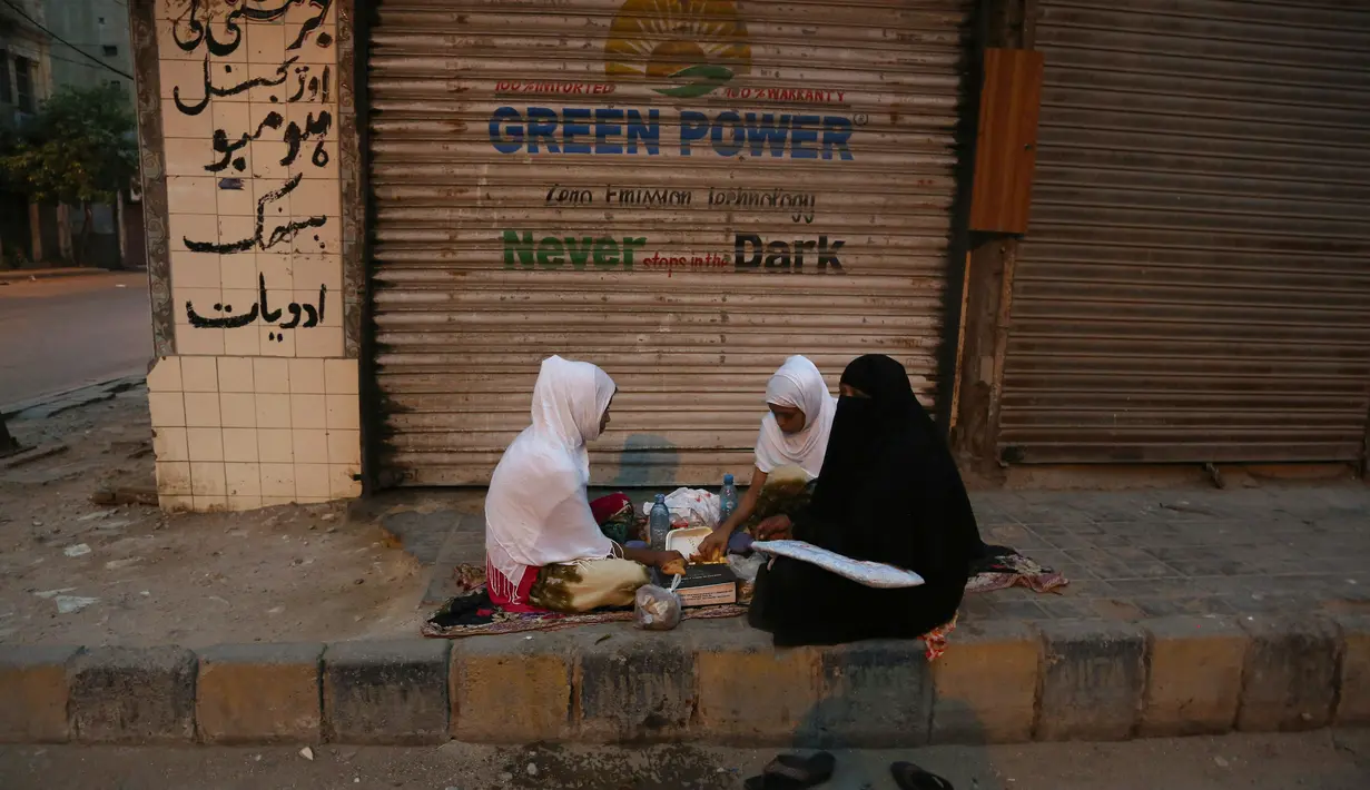 Sebuah keluarga berbuka puasa di trotoar setelah menerima makanan gratis selama pandemi Covid-19 di Karachi, Pakistan, Minggu, (10/5/2020). (AP/Fareed Khan)