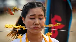 Seorang wanita menusuk pipinya dengan besi  saat mengikuti prosesi perayaan Festival Vegetarian tahunan di Phuket, Thailand, Kamis (3/10/2019). Festival menyiksa diri ini dipercaya bagi warga Phuket akan mendapat kesehatan dan ketenangan pikiran. (AFP Photo/Mladen Antonov)