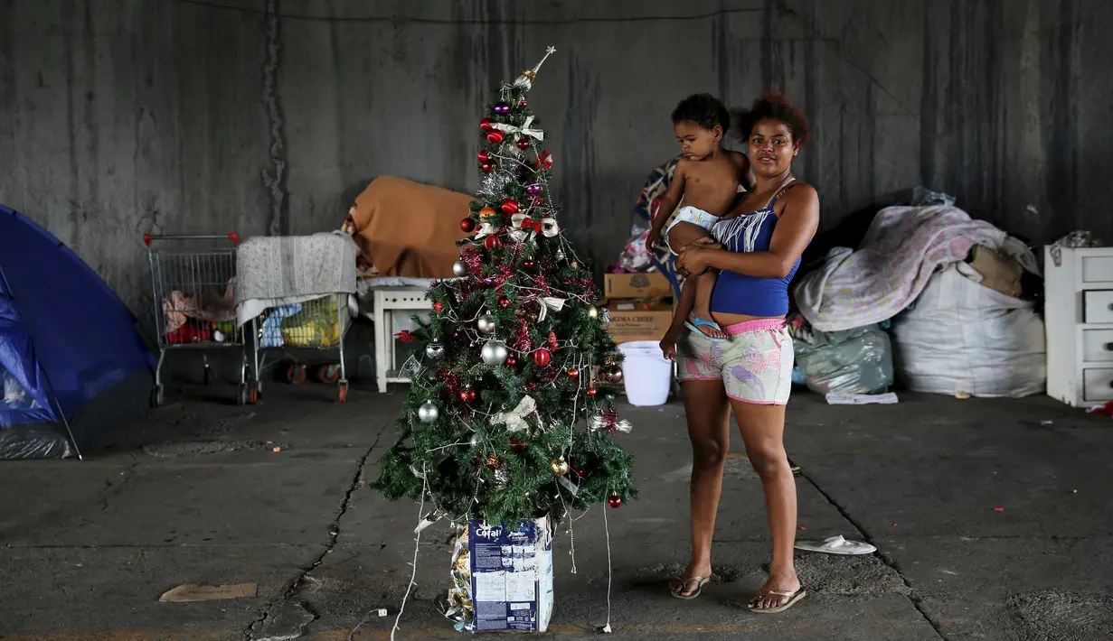 Camila (kanan) dan anaknya berpose disamping pohon Natal di Sao Paulo, Brasil, (18/12). Mereka adalah keluarga tunawisma yang tinggal di bawah jembatan. (REUTERS/Nacho Doce)