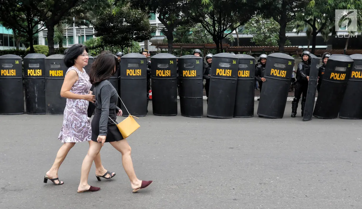 Pejalan kaki melintas di depan anggota polisi yang menggunakan tameng untuk menutup jalan pada peringatan Hari Buruh 2019 di kawasan Bundaran HI, Jakarta, Rabu (1/5/2019). Aparat kepolisian menutup Jalan Sudirman arah Bundaran HI atau sebelum Halte Transjakarta Tosari. (Liputan6.com/Johan Tallo)