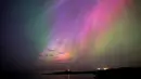 Aurora borealis, juga dikenal sebagai cahaya utara, bersinar di cakrawala di Mercusuar St Mary di Whitley Bay di pantai Timur Laut, Inggris, Jumat, 10 Mei 2024. (Owen Humphreys/PA via AP)