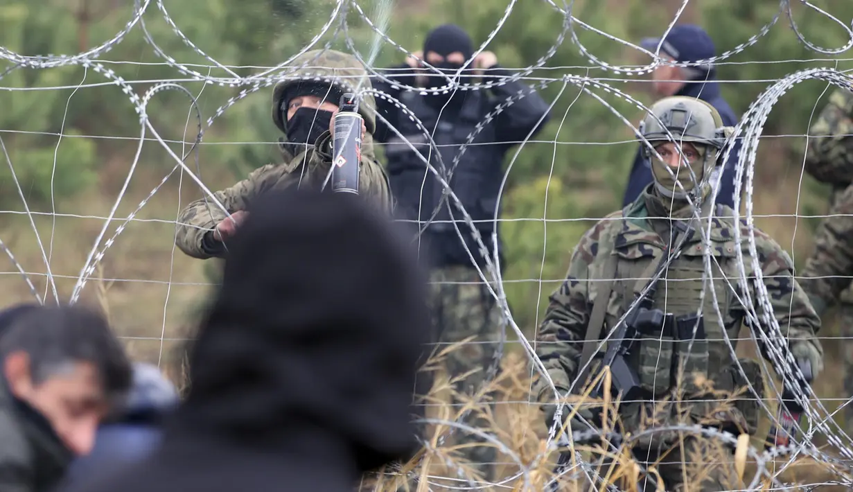Petugas Polandia berdiri di dekat kawat berduri ketika para migran dari Timur Tengah dan tempat lain berkumpul di perbatasan Belarus-Polandia dekat Grodno, Belarus, Senin (8/11/2021). Para migran awalnya berjalan melalui Lithuania dan Latvia dan sekarang terutama melalui Polandia. (Leonid Shcheglov/