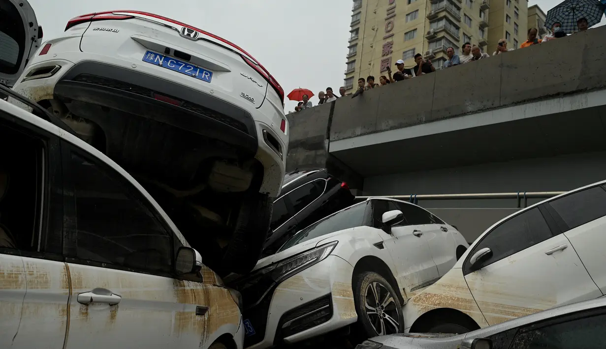 Orang-orang melihat mobil-mobil yang terendam banjir setelah hujan lebat melanda Zhengzhou di provinsi Henan, China, Kamis (22/7/2021). Para peramal cuaca mengatakan Zhengzhou mendapat curah hujan dalam setahun hanya dalam tiga hari. (Noel Celis/AFP)