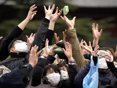 Orang-orang mencoba menangkap kacang keberuntungan yang disebarkan selama "Mame-maki", upacara melempar kacang, di kuil Buddha Zojoji, Tokyo, Jumat (3/2/2023). Ritual yang diyakini membawa keberuntungan dan mengusir kejahatan ini dilakukan setiap tahun untuk menandai awal musim semi dalam kalender lunar. (AP Photo/Eugene Hoshiko)