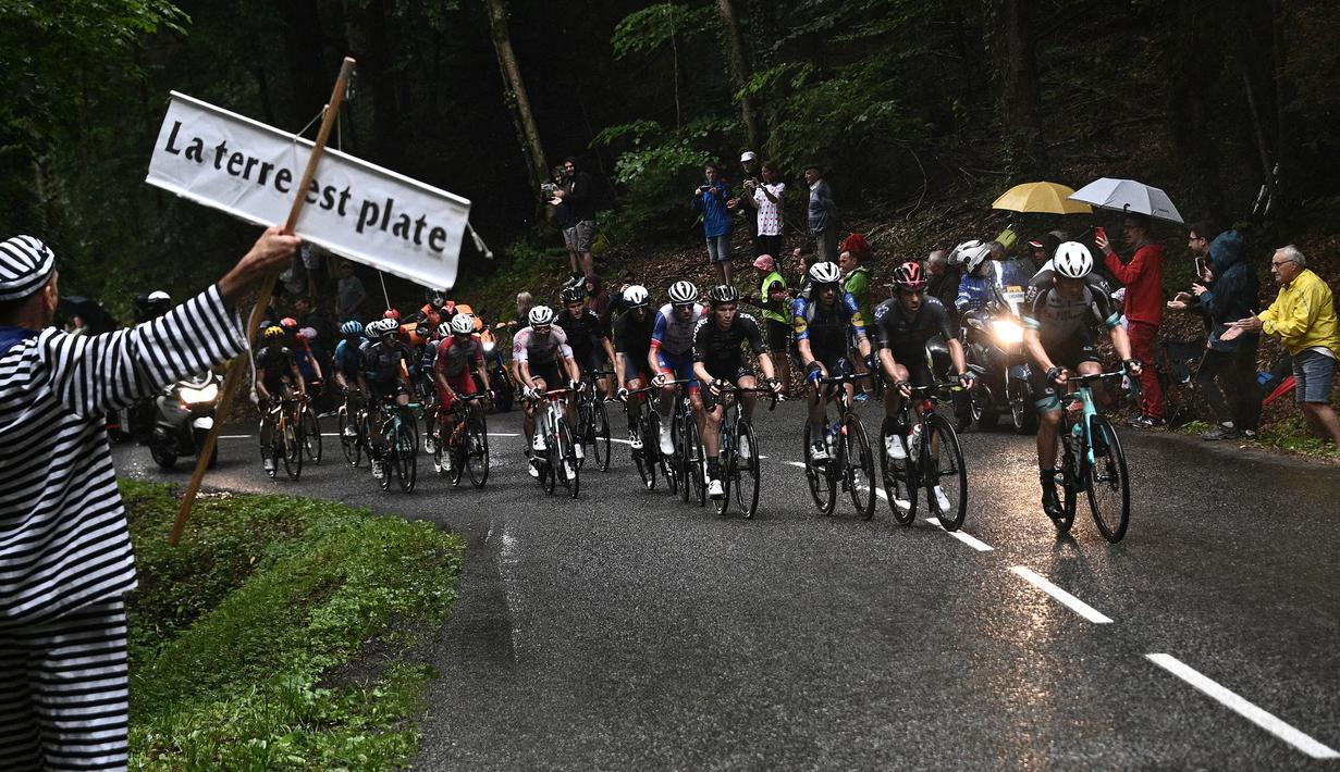 Rombongan pembalap melewati seorang penonton yang sedang memegang poster bertuliskan "Bumi itu datar" pada etape ke-8 balap sepeda Tour de France 2021 yang menempuh jarak 150 km, dari Oyonnax menuju Le Grand-Bornand, pada 03 Juli 2021. (AFP/Anne-Christine Poujoulat)