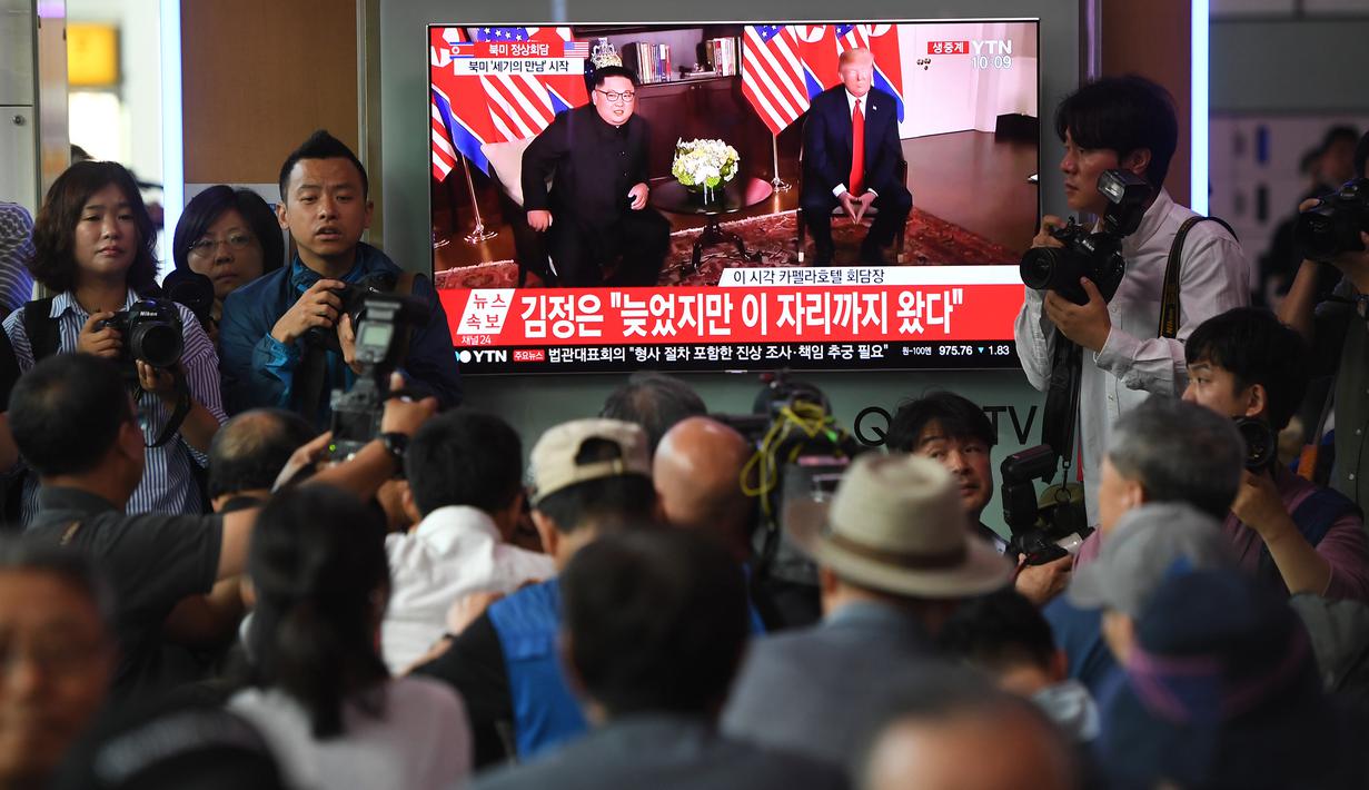 Calon penumpang dan awak media melihat berita pertemuan Presiden AS Donald Trump dan pemimpin Korea Utara Kim Jong-un di sebuah stasiun kereta api Seoul, Selasa (12/6). Untuk pertama kalinya dalam sejarah, Trump dan Kim bertemu. (AFP PHOTO/Jung Yeon-je)