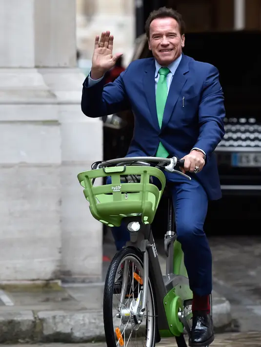 Gubernur California ke-38, Arnold Schwarzenegger tersenyum saat mengendarai sepeda untuk bertemu Walikota Paris, Anne HIdalgo di Paris (11/12). Schwarzenegger berada di Paris untuk menghadiri pertemuan puncak iklim One Planet.  (AFP Photo / Alain Jocard)