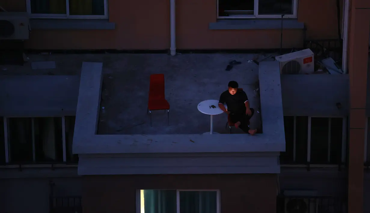 Seorang pria melihat smartphone-nya di balkon di sebuah komunitas perumahan di Shanghai, China (11/4/2022). AS telah memerintahkan semua staf konsuler non-darurat untuk meninggalkan Shanghai, yang berada di bawah penguncian ketat untuk menahan lonjakan COVID-19. (AP Photo)