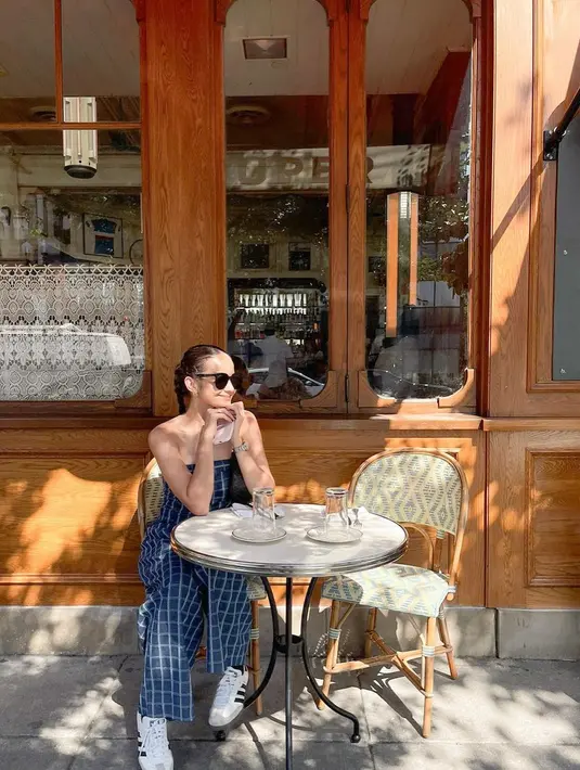 Gaya Enzy Storia menikmati waktunya dengan outfit chic. Strapless jumpsuit bermotif kotak berwarna biru, dipadu Enzy dengan sneakers putih dan sunglasses. [Foto: Instagram/enzystoria]