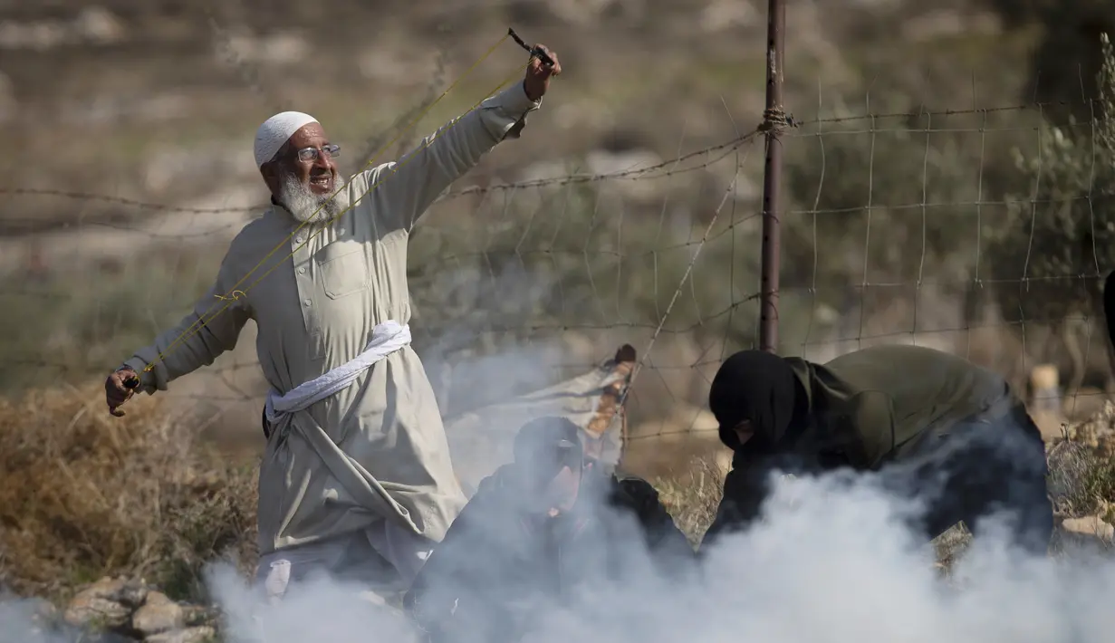 Seorang demonstran Palestina menggunakan ketapel untuk melemparkan batu ke arah pasukan Israel selama protes terhadap pemukiman Israel, di desa Deir Jarir Tepi Barat, utara Ramallah, Jumat (1/1/2021). (AP Photo/Majdi Mohammed)