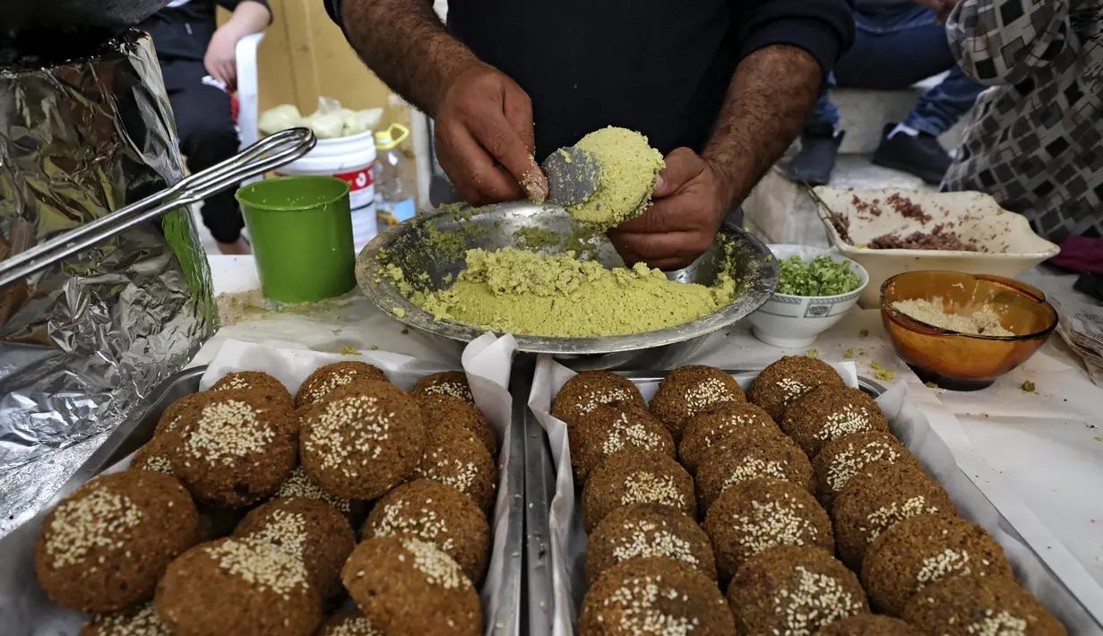 Seorang pedagang Palestina menyiapkan patty falafel di stannya di kota Hebron di Tepi Barat yang diduduki, selama bulan suci Ramadhan, Minggu (18/4/2021). Falafel adalah sebuah makanan Timur Tengah yang pada bulan Ramadhan, sering dimakan sebagai hidangan buka puasa. (HAZEM BADER/AFP)