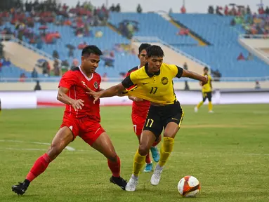 Gelandang Timnas Indonesia U-23, Asnawi Mangkualam berusaha merebut bola dari bek Malaysia, Muhammad Safwan bin Mazlan dalam pertandingan perebutan medali perunggu SEA Games 2021 di Stadion My Dinh, Minggu (22/5/2022). Indonesia ditahan imbang 1-1 dan menang 4-3 di adu penalti. (AFP/Tang Chhin Sothy)