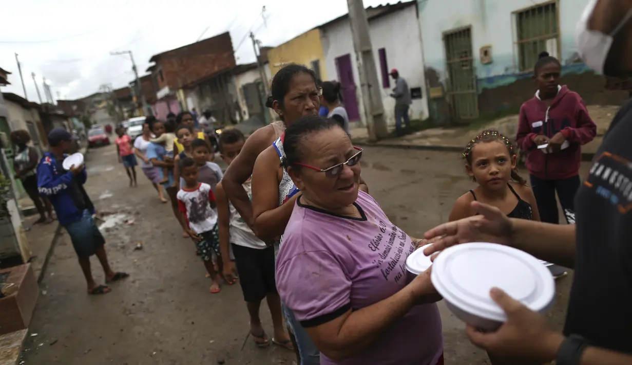 Warga yang terkena banjir mengantre untuk makanan yang disumbangkan di Itapetinga, negara bagian Bahia, Brasil, Selasa (28/12/2021). Banjir menyebabkan ribuan orang terpaksa mengungsi dari rumah mereka . (AP/Raphael Muller)