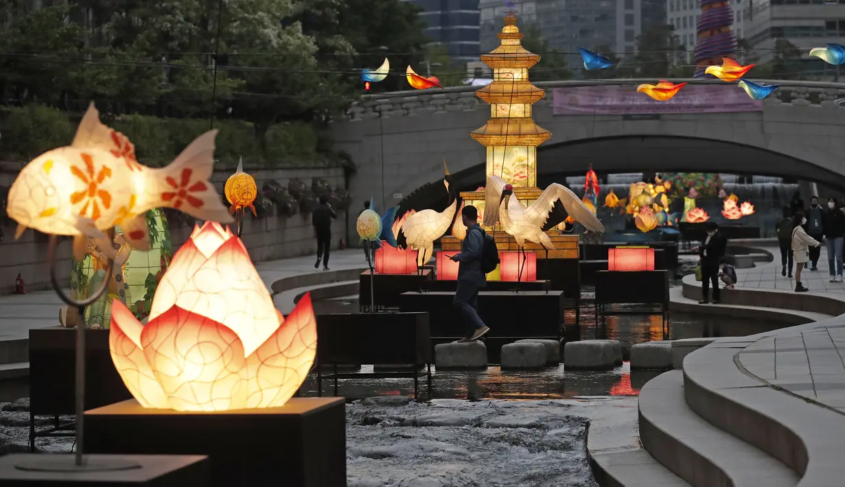 Pengunjung yang mengenakan masker wajah sebagai tindakan pencegahan penyebaran virus corona COVID-19 berjalan dekat lentera yang dipajang untuk perayaan ulang tahun Buddha pada 19 Mei mendatang di Seoul, Korea Selatan, Senin (10/5/2021). (AP Photo/Lee Jin-man)