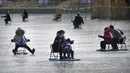 Seorang wanita dan anak-anak mendorong kursi es melintasi kolam beku di taman umum di Beijing, Selasa (17/1/2023). China telah mengumumkan penurunan populasi pertamanya dalam beberapa dasawarsa seiring bertambahnya usia negara terpadat di dunia dan angka kelahirannya yang menurun. (AP Photo/Mark Schiefelbein)