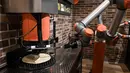 Robot pembuat pizza Bernama "Pazzi" terlihat sedang bekerja di sebuah restoran di Paris pada 1 Juli 2021. Pazzi dapat menjadi cikal bakal pasukan robot koki masa depan di seluruh dunia. (BERTRAND GUAY/AFP)