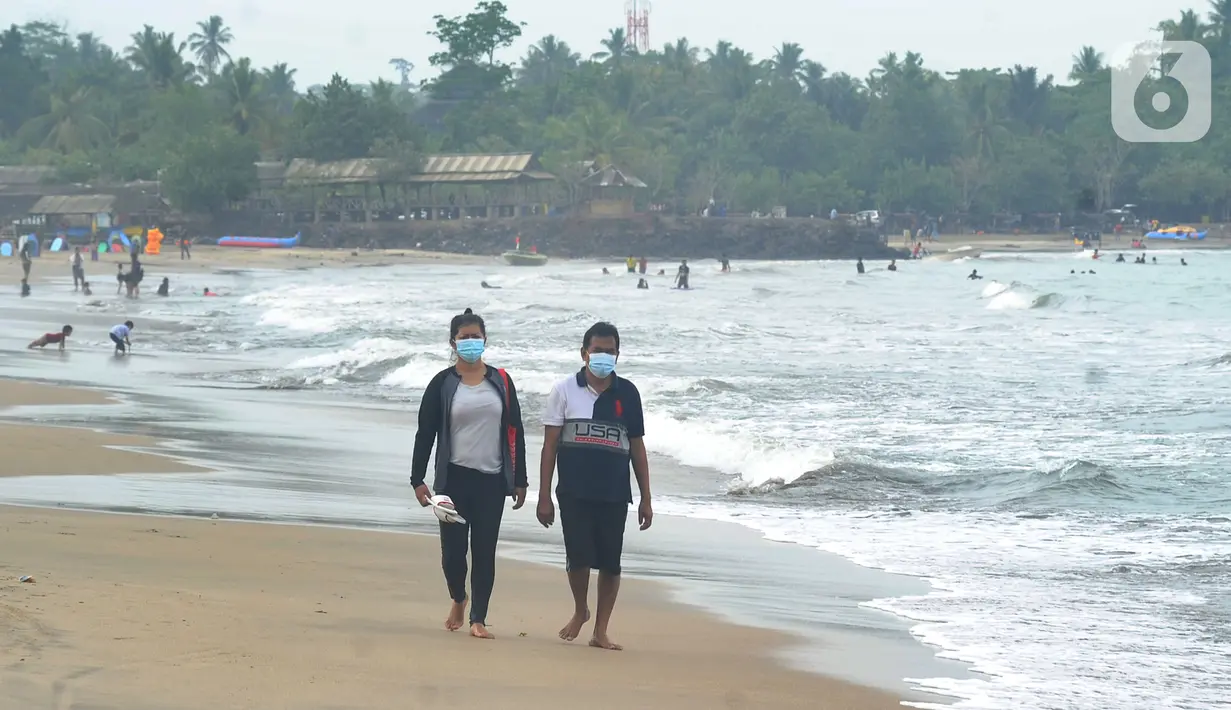 Wisatawan yang mengenakan masker menikmati suasana Pantai Anyer di Cilegon, Banten, Minggu (25/10/2020). Akhir pekan dimanfaatkan warga Jakarta dan sekitarnya untuk berwisata dengan tetap menerapkan protokol kesehatan Covid-19. (merdeka.com/Arie Basuki)