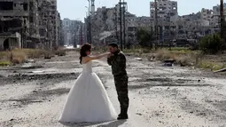 Pasangan pengantin baru, Hassan Youssef (27) tampak menghadap  pengantin wanita, Nada Merhi (18), sambil mencium tangan pasangannya dengan latar belakang pemandangan tandus kota Homs yang menjadi medan perang di Suriah, 5 Februari 2016. (JOSEPH EID/AFP)
