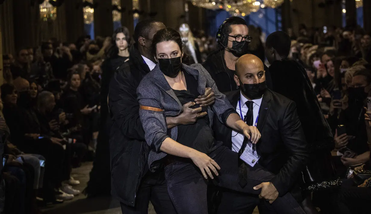 Seorang pengunjuk rasa dikeluarkan dari runway peragaan busana Louis Vuitton Spring/Summer 2022 di Paris, Selasa (5/10/2021). Membentangkan spanduk, pengunjuk rasa itu berbaris di jalan yang sama dengan para model. (Vianney Le Caer/Invision/AP)