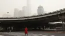 Seorang wanita menyeberang jalan dekat gedung pencakar langit saat badai pasir di Beijing (28/3/2021). Badai pasir kembali menyapu Beijing pada Minggu (28/3), mengubah langit menjadi kuning, membatasi jarak pandang dan mengganggu lalu lintas. (AP Photo/Ng Han Guan)