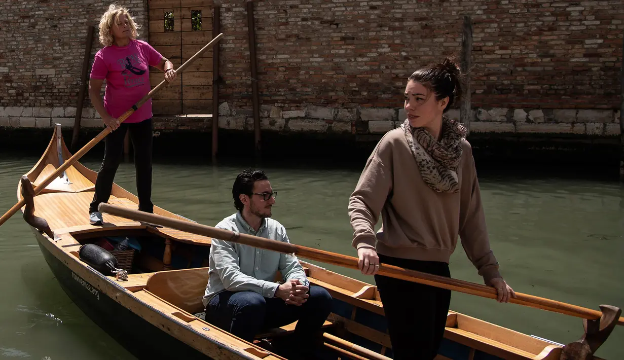 Gabriella Lazzari (kiri), anggota Row Venice, mengajarkan mendayung gondola bagi wisatawan di sebuah kanal di Venesia, Italia pada 16 Mei 2019. Pengalaman ini bisa dimiliki dengan sekitar Rp 1,37 juta per gondola selama 90 menit untuk empat orang yang dimulai pukul 10.00 pagi. (MARCO BERTORELLO/AFP)
