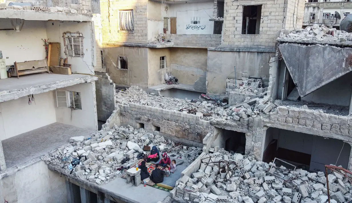 Keluarga Tareq Abu Ziad menunggu waktu berbuka puasa di tengah reruntuhan rumah mereka yang hancur setelah serangan militer pasukan pemerintah dan sekutunya di Kota Ariha, Provinsi Idlib, Suriah, Senin (4/5/2020). Muslim Suriah melewati Ramadan tahun ini masih dalam kondisi perang. (AAREF WATAD/AFP)