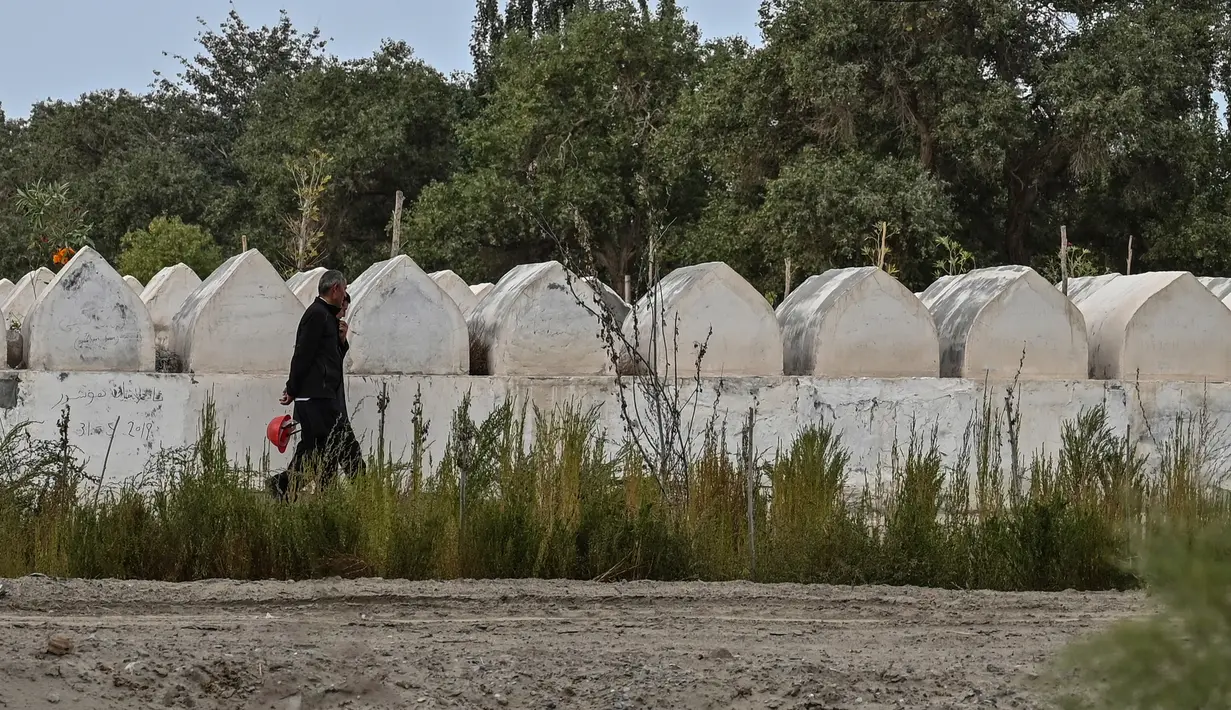 Gambar pada 12 September 2019 menunjukkan  orang-orang berjalan dekat pemakaman etnis Uighur di Shayar, wilayah Xinjiang. Mengambil data satelit Earthrise Alliance, puluhan situs pemakaman Uighur di Xinjiang telah dihancurkan dalam kurun waktu dua tahun. (HECTOR RETAMAL/AFP)