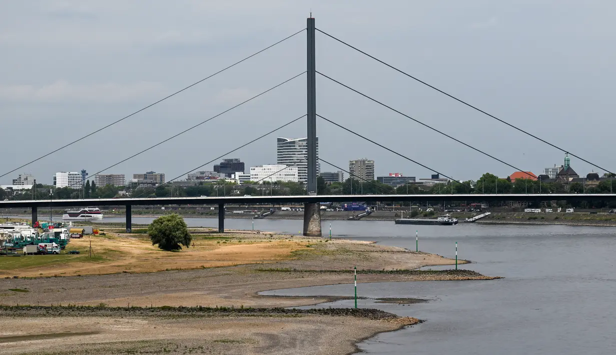 <p>Sebuah kapal pedalaman berlayar di Rhine saat orang-orang berdiri di pantai di tepi sungai yang sebagian mengering di Duesseldorf, Jerman barat (25/7/2022). Keringnya sungah Rhine akibat Eropa mengalami gelombang panas. (AFP/Photo/Ina Fassbender)</p>