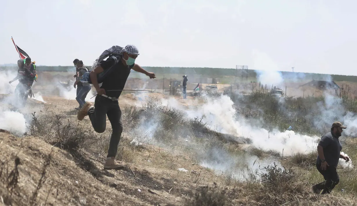 Warga Palestina berlindung dari tembakkan gas air mata pasukan Israel di perbatasan Jalur Gaza dengan Israel, (6/4). Aksi ini bertujuan untuk merebut kembali tanah kelahiran mereka yang direnggut Israel tujuh dekade silam. (AP Photo/Khalil Hamra)