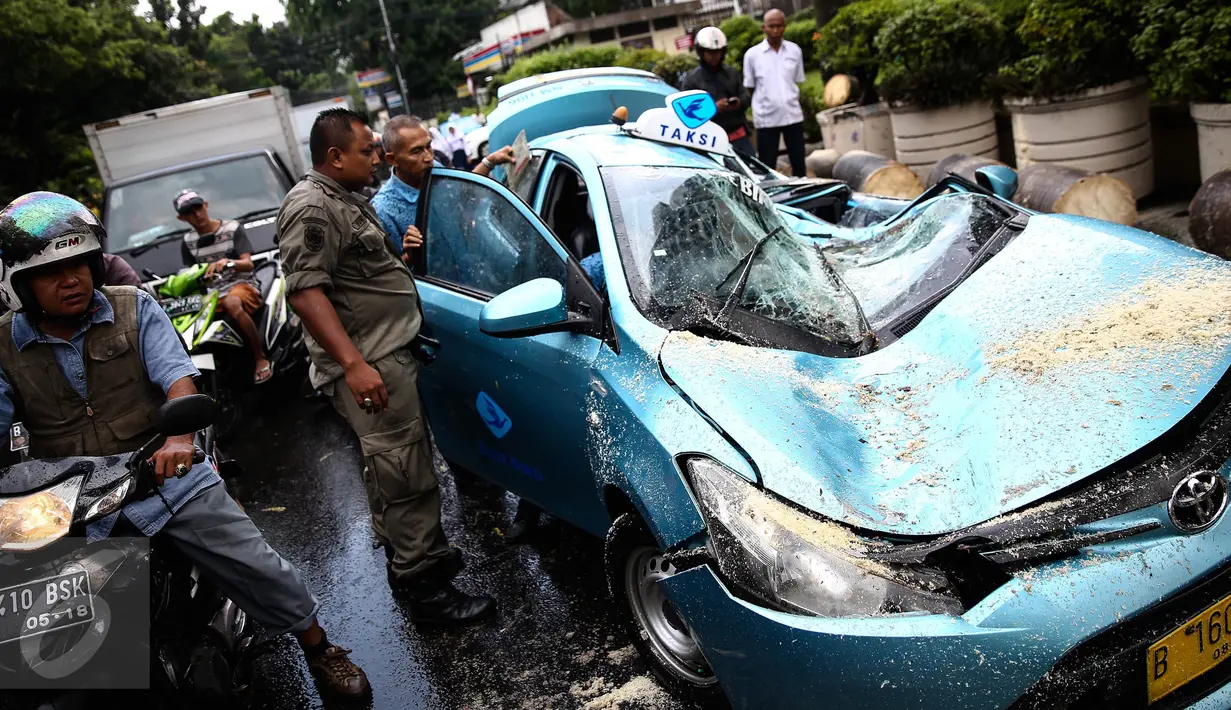 Petugas bersama sopir taksi memeriksa kondisi taksi yang tertimpa pohon tumbang di dekat Hotel Millenium, Jalan Taman Kebon Sirih, Jakarta, Selasa (30/8). Pohon itu roboh menimpa taksi bernopol B 1606 TTC hingga ringsek berat. (Liputan6.com/Faizal Fanani)