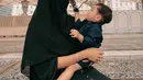 Potret gemas, Paula Verhoeven yang menjalankan ibadah Umroh membawa sang buah hati. Di foto ini, ia menggendong anak keduanya, mengenakan gamis hitam polos dan hijab bercadar yang serasi. [Foto: Instagram/paula_verhoeven]