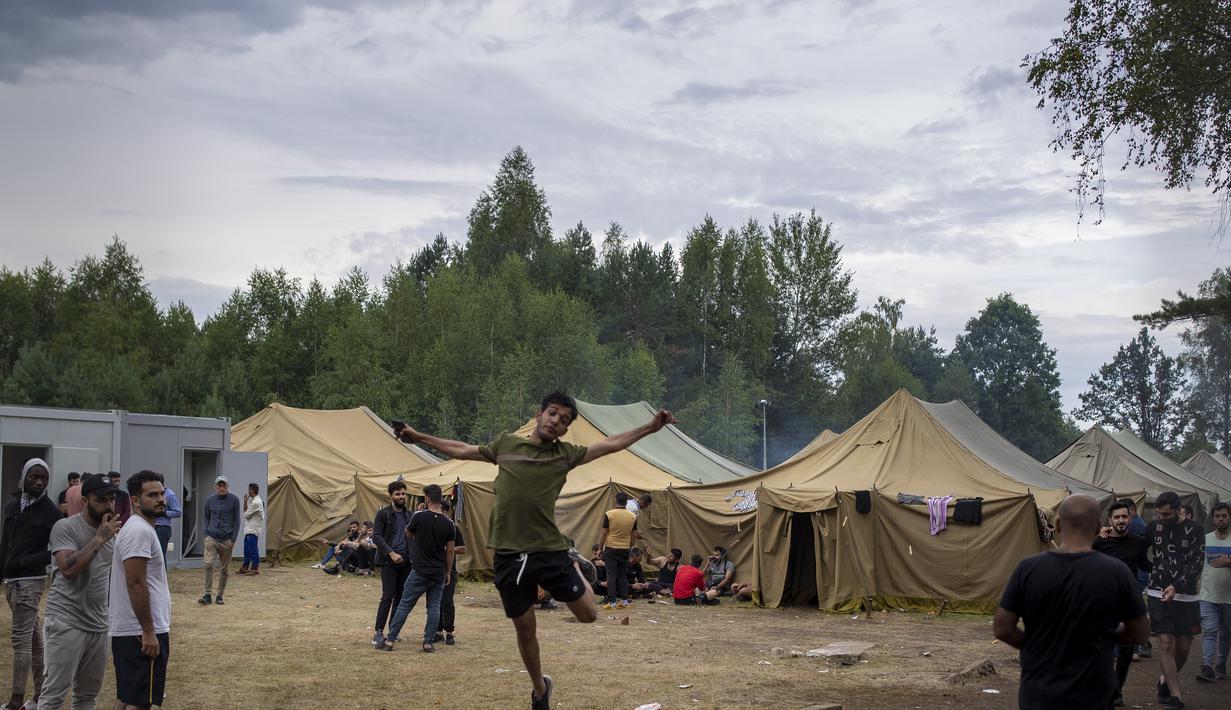 Seorang migran melompat ketika yang lain berjalan di dalam kamp pengungsi yang baru dibangun di tempat latihan militer Rudninkai, sekitar 38 km (23,6 mil) selatan dari Vilnius, Lithuania, Rabu (4/8/2021). (AP Photo/Mindaugas Kulbis)
