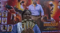 Seorang penggemar memperlihatkan tiket filmnya di dekat poster superstar India Rajinikanth, di luar gedung bioskop untuk merayakan pemutaran film terbarunya "Jailer" di Mumbai, India, Kamis (10/8/2023). (AP Photo/Rafiq Maqbool)