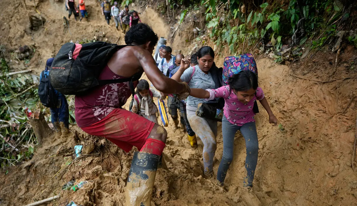 Seorang Migran membantu  anak-anak saat berjalan melewati jalanan berlumpur melintasi Celah Darien dari Kolombia ke Panama,  Sabtu, (15/10/2022). Perjalanan Kelompok Imigran tersebut berharap mencapai Amerika Srikat (AS).(Fernando Vergara/AP)