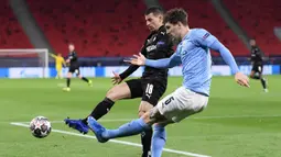 Bek Manchester City, John Stones (kanan) membuang bola dari ancaman bek Borussia Moenchengladbach, Stefan Lainer dalam laga leg kedua babak 16 besar Liga Champions 2020/2021 di Puskas Arena, Budapest, Selasa (16/3/2021). Manchester City menang 2-0 atas Gladbach. (AFP/Attila Kisbenedek)