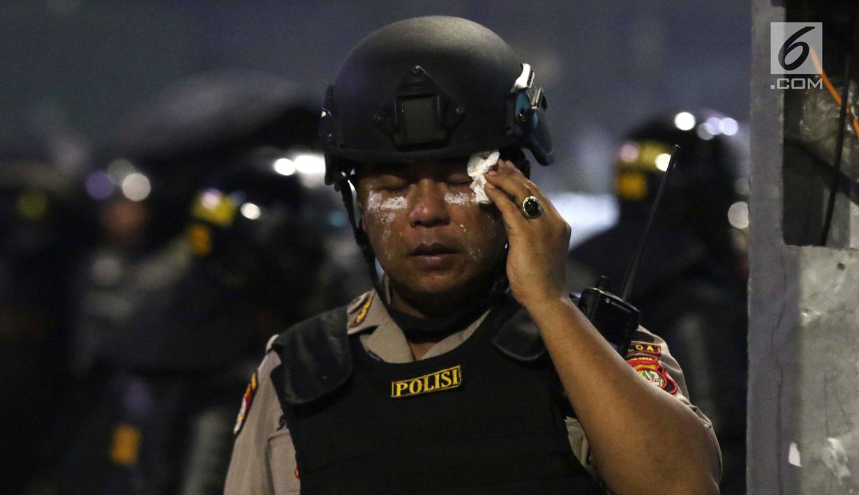 Personil Kepolisian dari satuan Brimob membasuh wajah rekannya yang terkena gas air mata saat menghalau massa yang berlaku anarkis di sekitar depan Gedung Bawaslu, Jalan MH Thamrin, Jakarta, Rabu (22/5/2019). (Liputan6.com/HelmiFithriansyah)