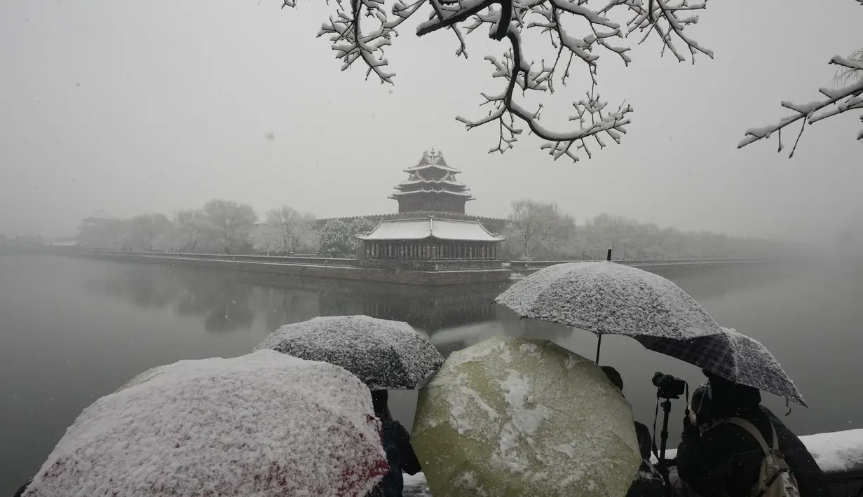 Pengunjung berkerumun untuk mengambil foto di tempat yang indah untuk Kota Terlarang saat salju turun di Beijing, China (18/3/2022). Gelombang dingin melanda banyak bagian China, menyebabkan suhu turun dan mengganggu lalu lintas di daerah yang terkena dampak. (AP Photo/Ng Han Guan)