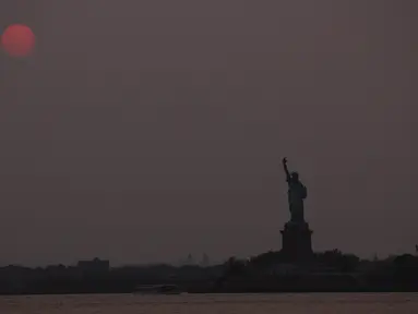 Matahari terbenam di atas Patung Liberty di New York City, Amerika Serikat pada 22 Mei 2023. (Spencer Platt/Getty Images/AFP)