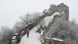 Seorang perempuan berjalan di Tembok Besar China setelah hujan salju ringan di Jiankou, utara Beijing pada Minggu (9/1/2022). Jalur pada Tembok Besar China itu pun terlihat memutih akibat salju. (GREG BAKER / AFP)
