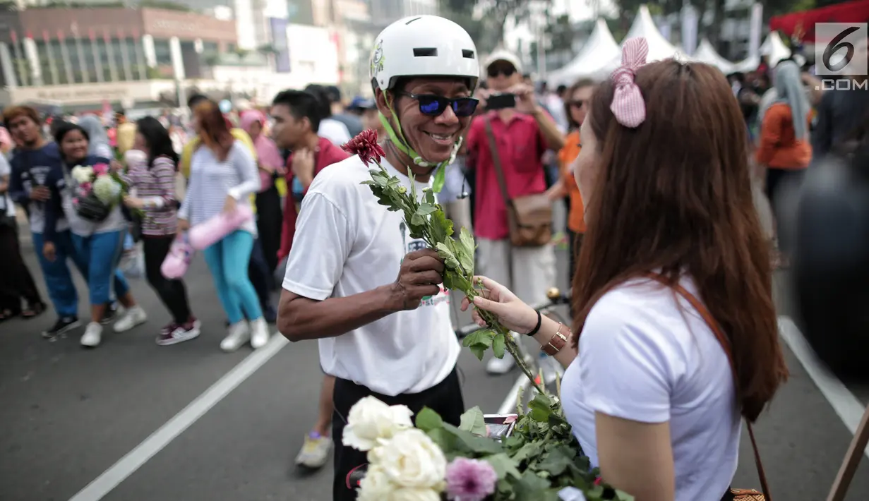 Anggota TKN Milenial Jokowi-Ma'ruf membagikan bunga kepada pengunjung car free day dalam kegiatan tabur bunga di Bundaran HI, Jakarta, Minggu (28/4/2019). Mereka mengajak masyarakat untuk ikut mengungkapkan duka atas meninggalnya 272 petugas KPPS dalam Pemilu 2019. (Liputan6.com/Faizal Fanani)