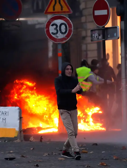 Demonstran berjalan dekat api saat kerusuhan menentang kenaikan harga bahan bakar di Paris, Prancis, Sabtu (24/11). Demonstran tersulut oleh hasutan beberapa oknum sehingga memicu kerusuhan. (AP Photo/Christophe Ena)